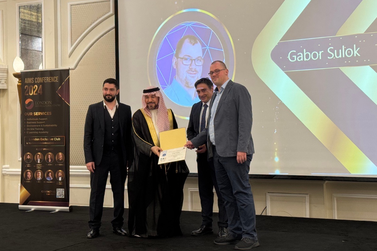 Elismerés átadása a színpadon az AIMS Dubai 2024 konferencián, a kivetítőn Sulok Gábor neve